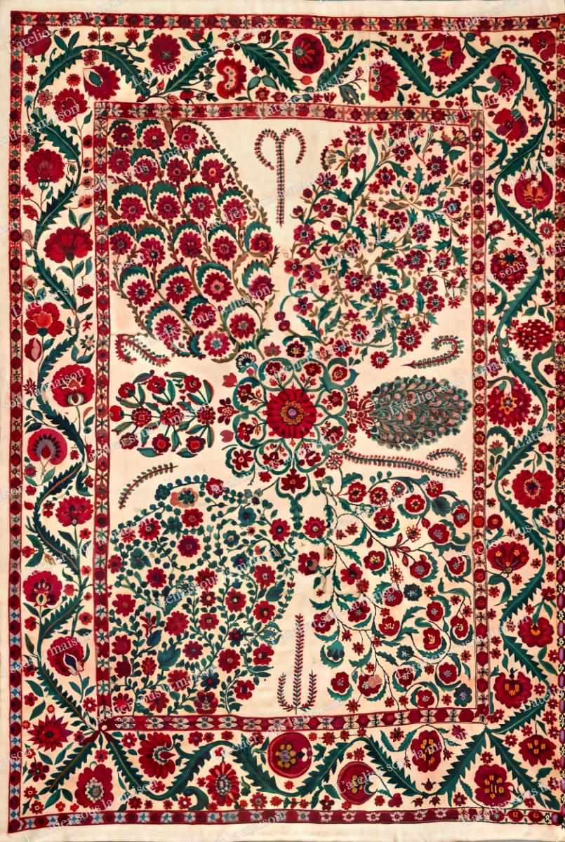 Grandes gerbes et rosaces rouges et vertes brodées sur fond écru, dans une bordure de fleurs et de feuillages.